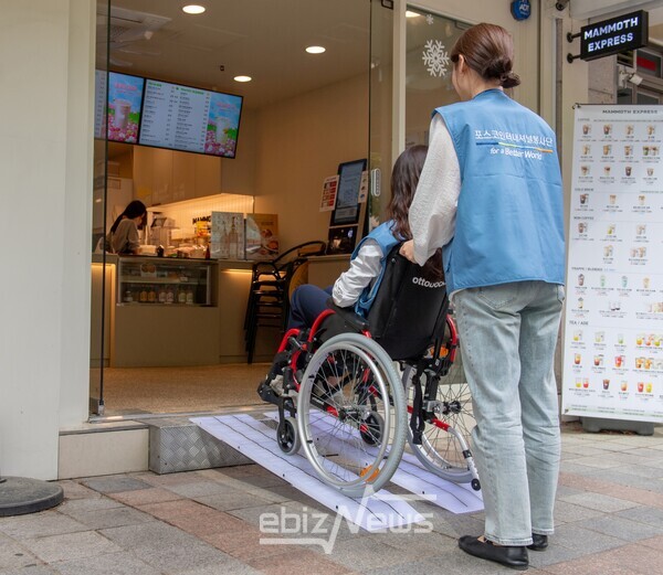 포스코인터내셔널 임직원들이 직접 휠체어를 타고 플라스틱 병뚜껑을 재활용해 만든 휠체어 이동식 경사로가 기증된 매장을 방문해 보고 있다.